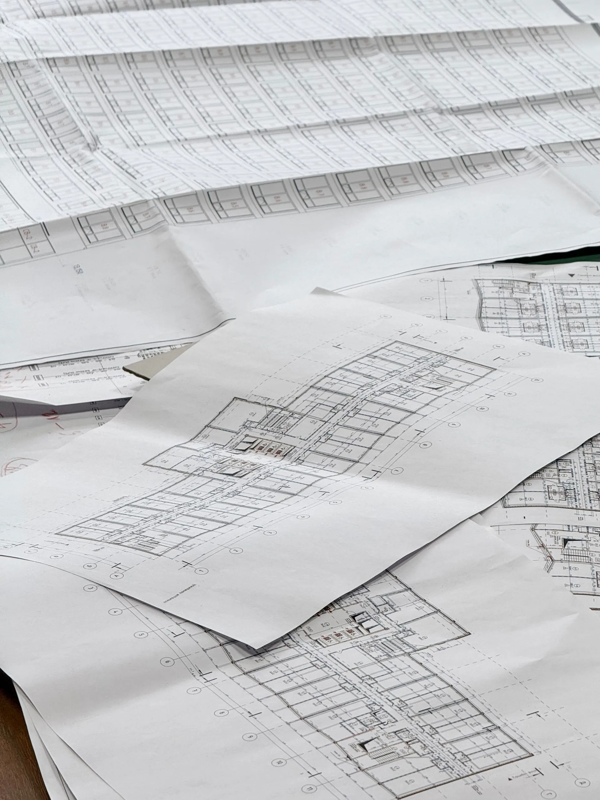 Plans techniques empilés et dépliés sur une table de travail, tracés au trait fin