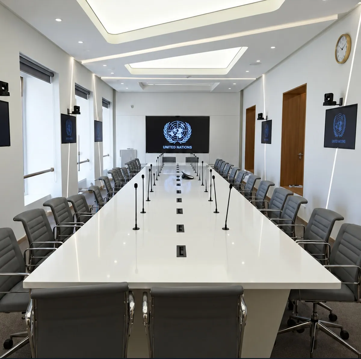 Salle de conférence de l'ONU après rénovation, table en fer à cheval équipée de micros et éclairage de plafond encastré