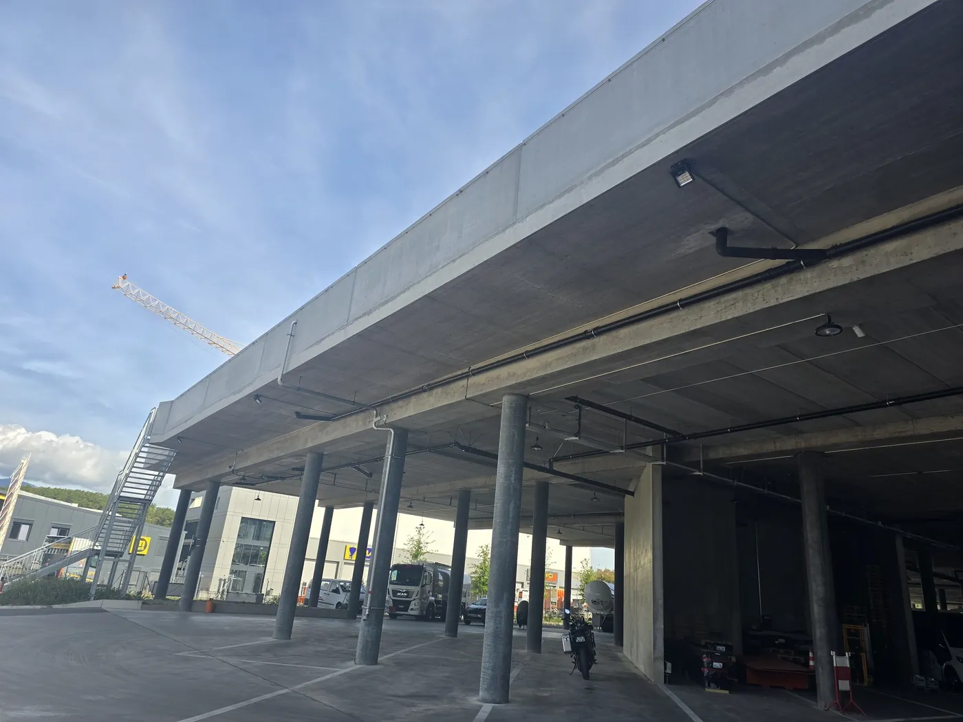 Auvent en béton d'un bâtiment logistique, poteaux alignés et zone de manoeuvre pour véhicules utilitaires